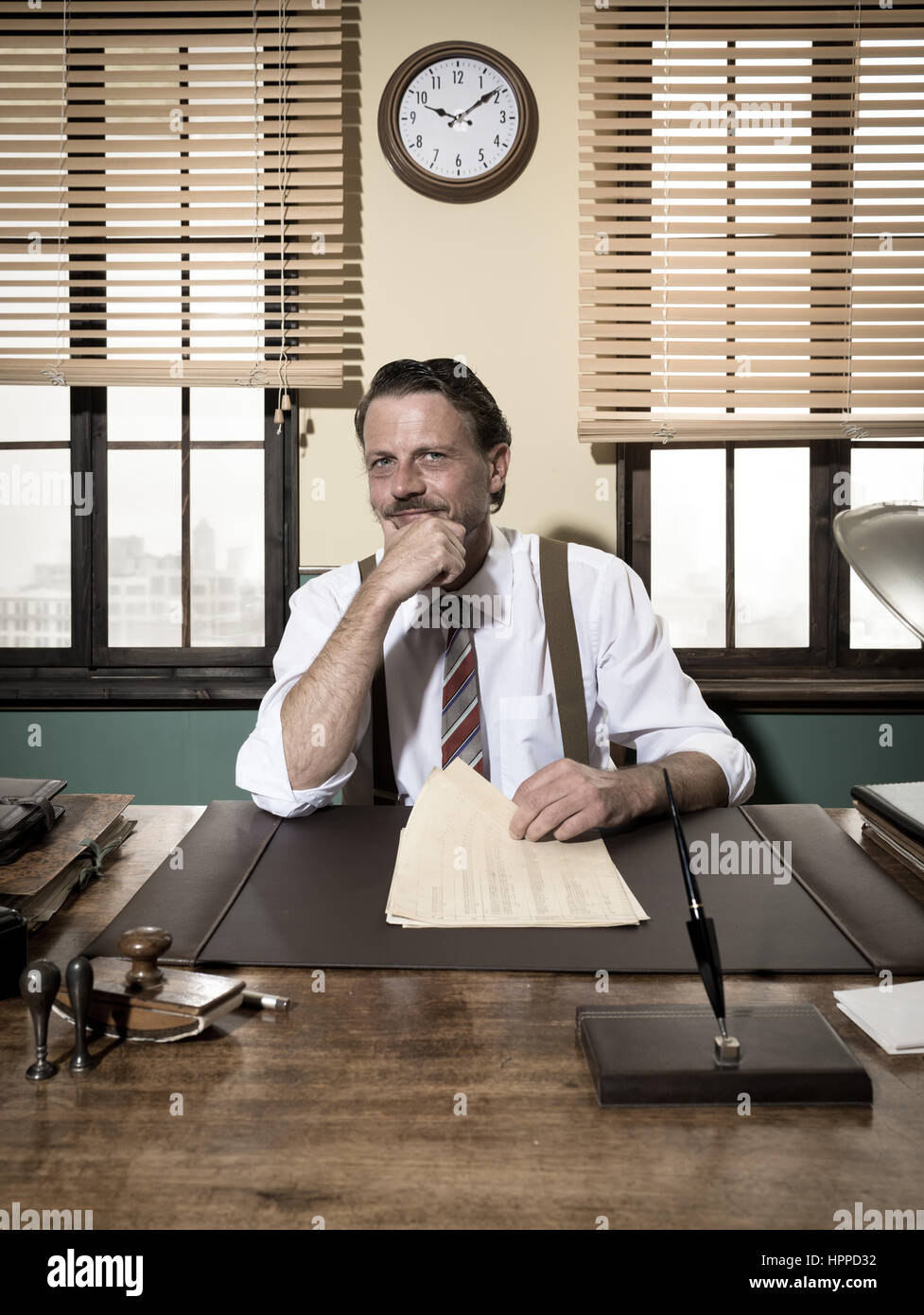 Confiant smiling businessman working at office desk with hand on chin. Banque D'Images Confiant smiling businessman working at office desk with hand on chin. Banque D'Images