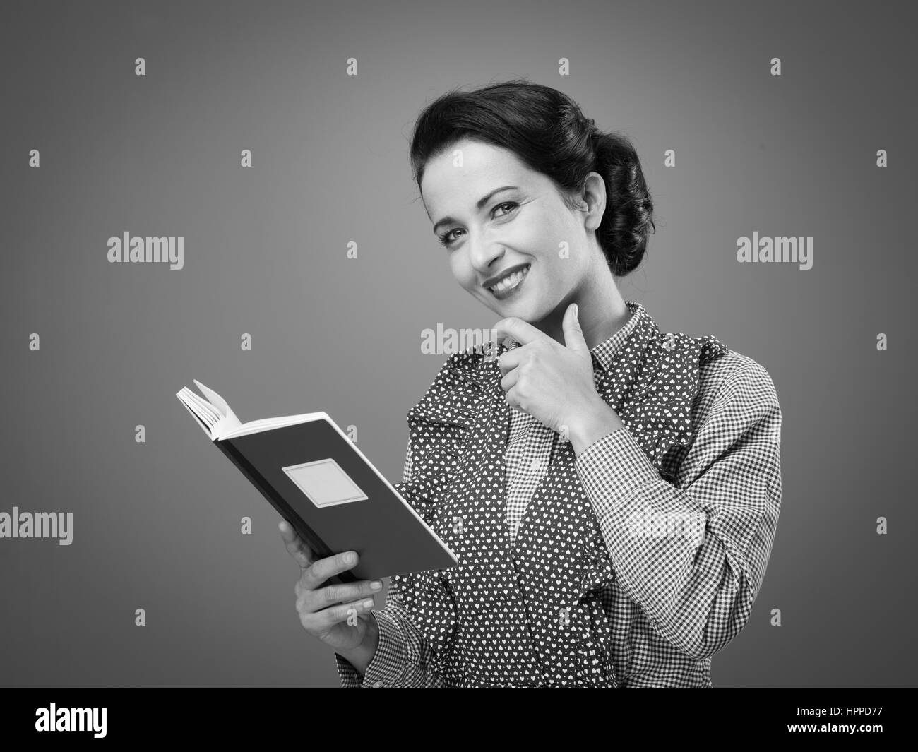 Rétro femme en souriant avec tablier et livre de hand on chin Banque D'Images Rétro femme en souriant avec tablier et livre de hand on chin Banque D'Images