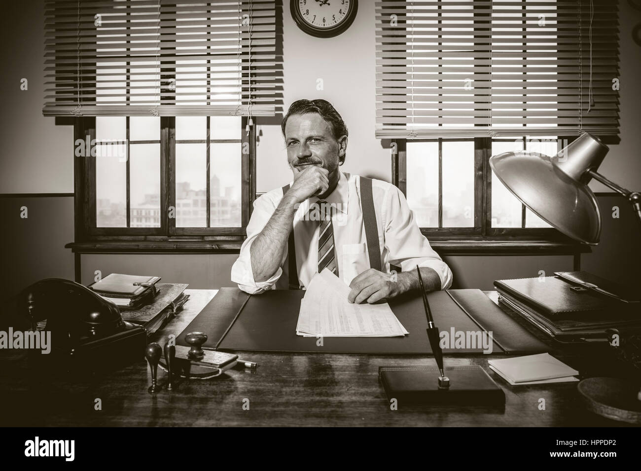 Confiant smiling businessman working at office desk with hand on chin. Banque D'Images Confiant smiling businessman working at office desk with hand on chin. Banque D'Images