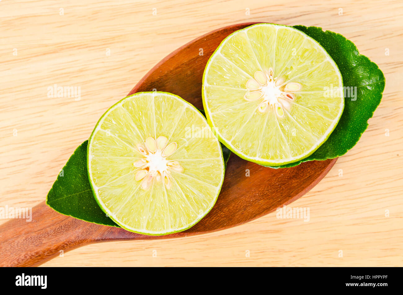 Tranche de citron vert avec une cuillère en bois en feuilles sur fond de bois. Banque D'Images