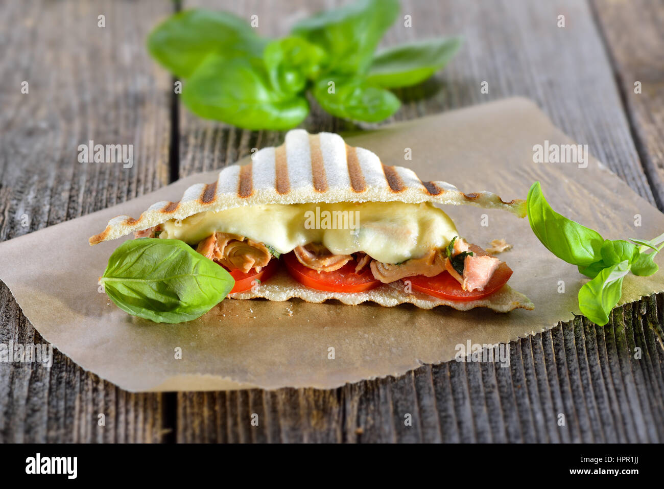 Panini grillé au thon, tomates, mozzarella et basilic frais fondu servi sur du papier sandwich sur une table en bois Banque D'Images