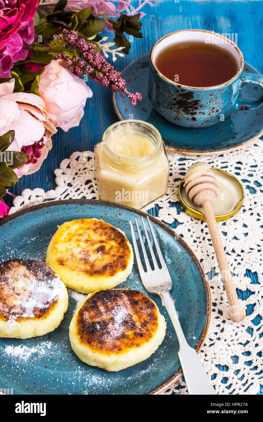 Beignets de fromage cottage, de miel et de thé dans une tasse d'époque sur un fond bleu. Studio Photo Banque D'Images