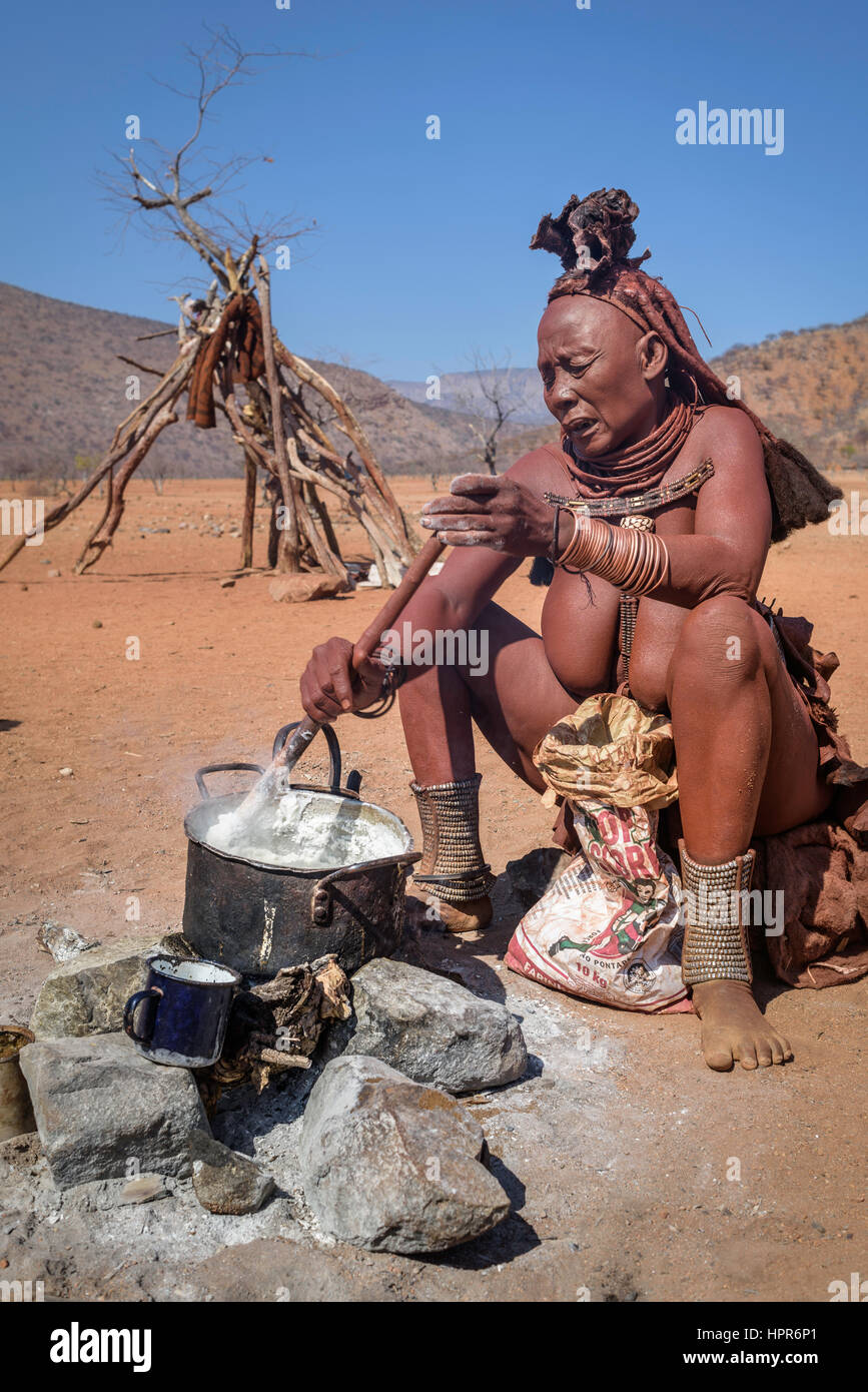 Vieille Femme Himba cuisson sur le feu un repas africain traditionnel fabriqué à partir de farine de maïs et l'eau. Banque D'Images