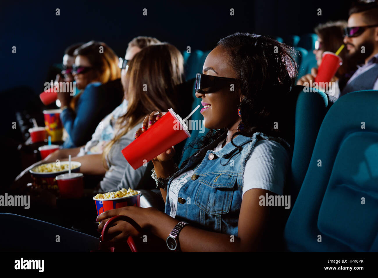Ravie de voir le nouveau film. Jeune femme africaine en sirotant son verre en regardant un film au cinema Banque D'Images