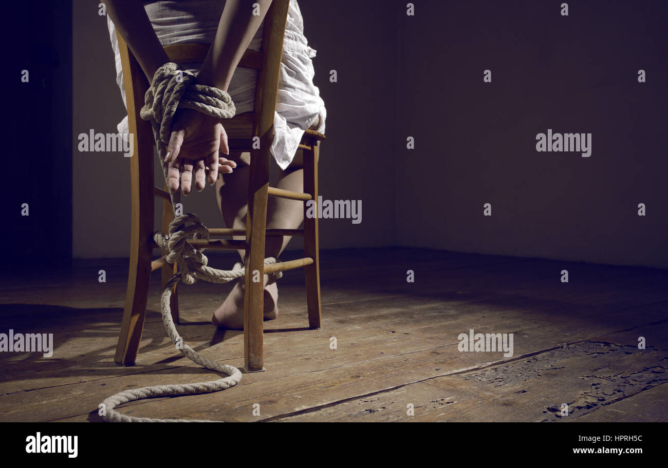 Jeune femme attachée à une chaise dans une salle vide Banque D'Images