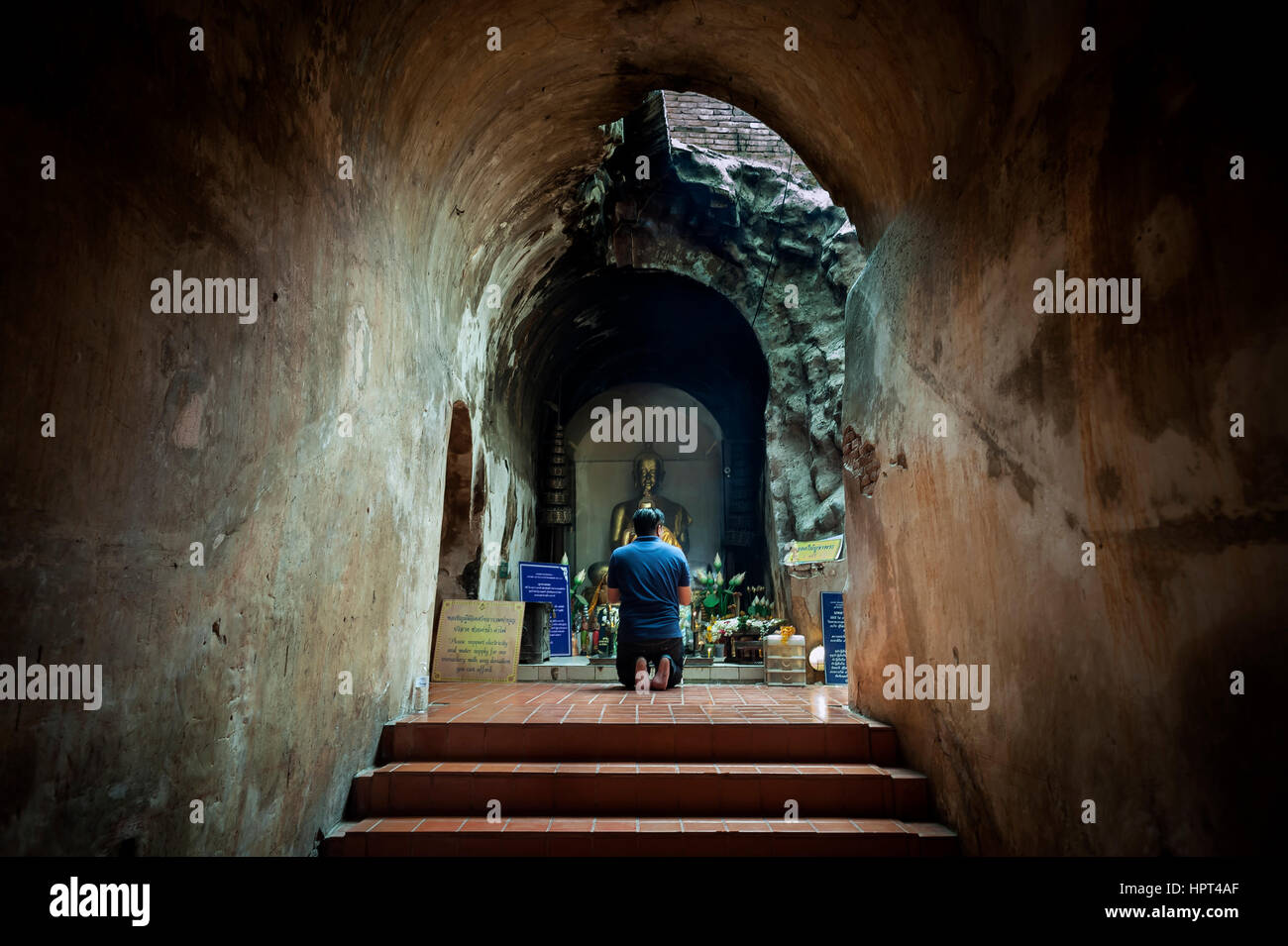 WAT UMONG, CHIANG MAI, THAÏLANDE - Juin 2015 - Un homme à genoux en prière devant une statue de Bouddha d'or à un autel souterrain à Wat Umong, Chiang Mai Banque D'Images