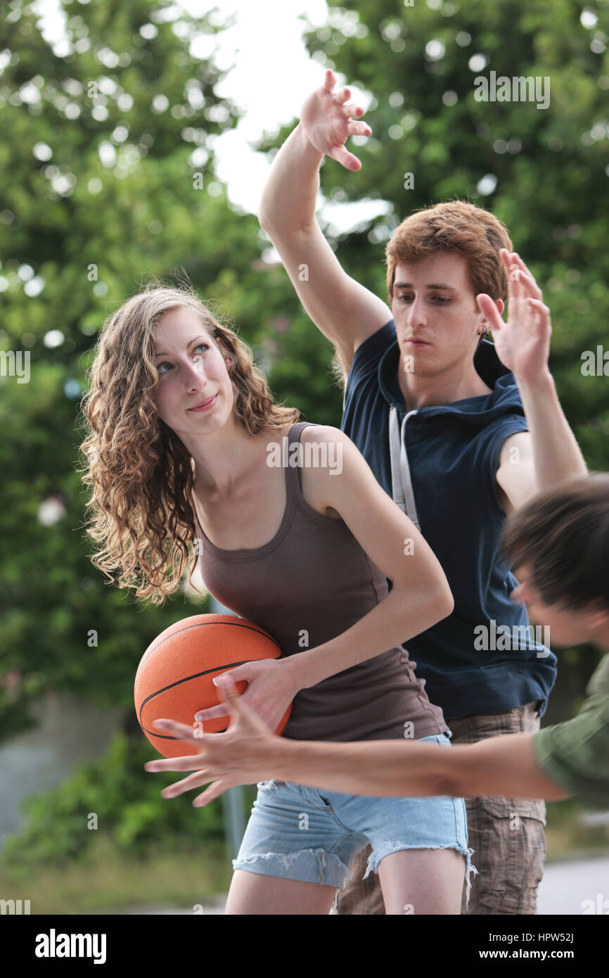 Deux garçons et une fille de jouer à un jeu de basket-ball sur une cour extérieure. Banque D'Images
