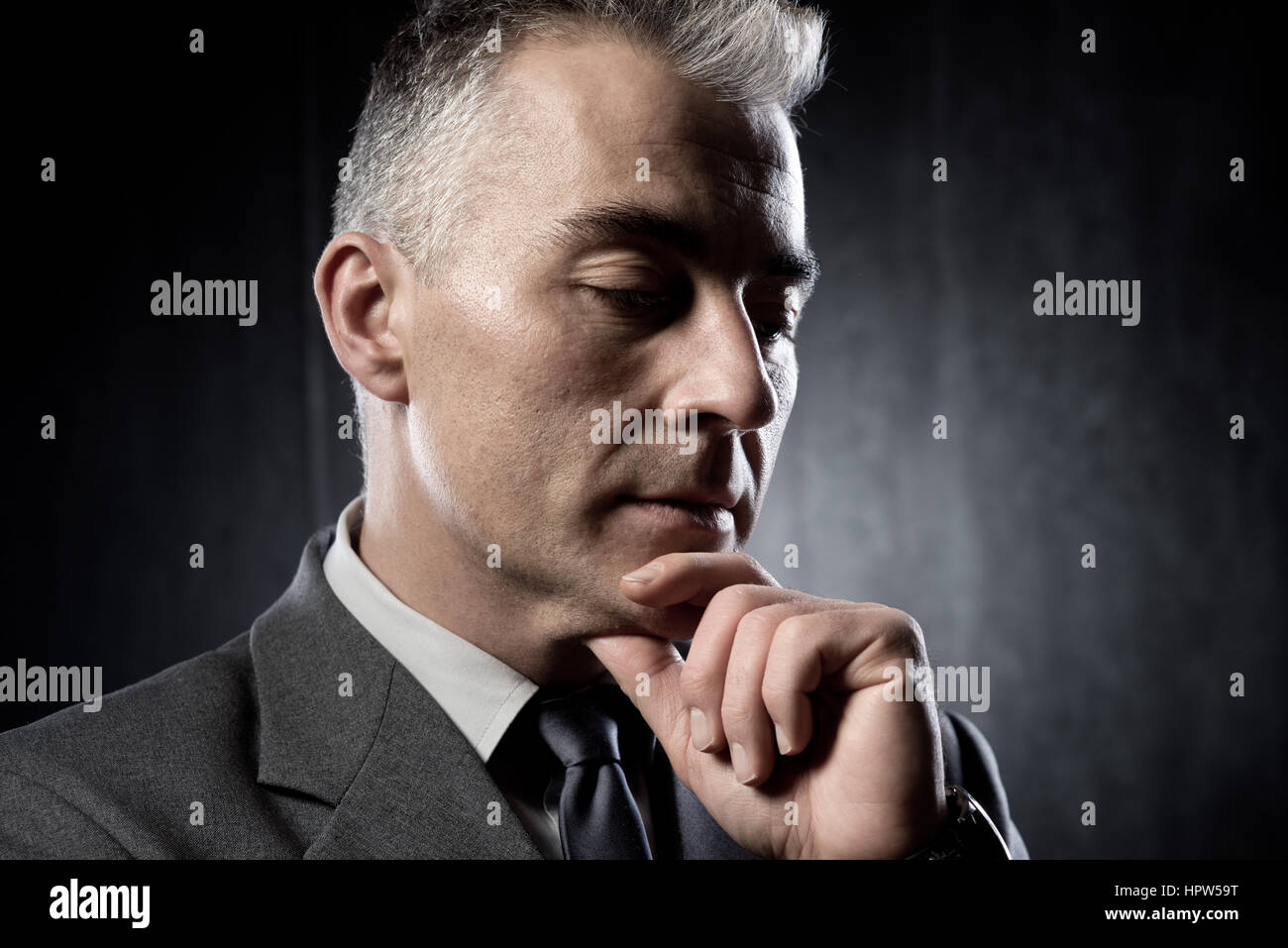 Pensive businessman with hand on chin sur fond sombre. Banque D'Images Pensive businessman with hand on chin sur fond sombre. Banque D'Images
