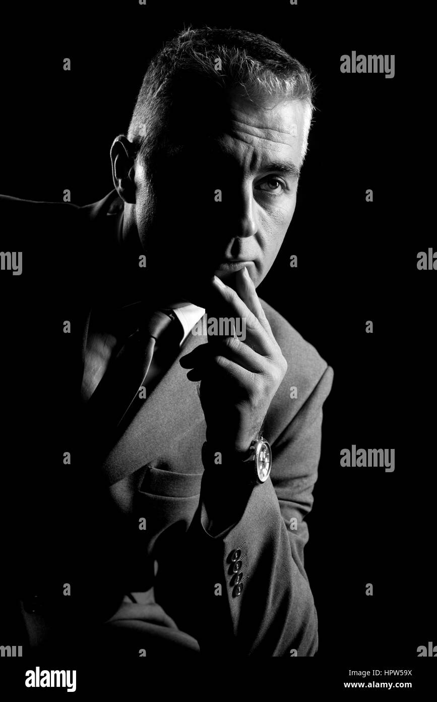 Confident businessman thinking with hand on chin sur fond sombre. Banque D'Images Confident businessman thinking with hand on chin sur fond sombre. Banque D'Images