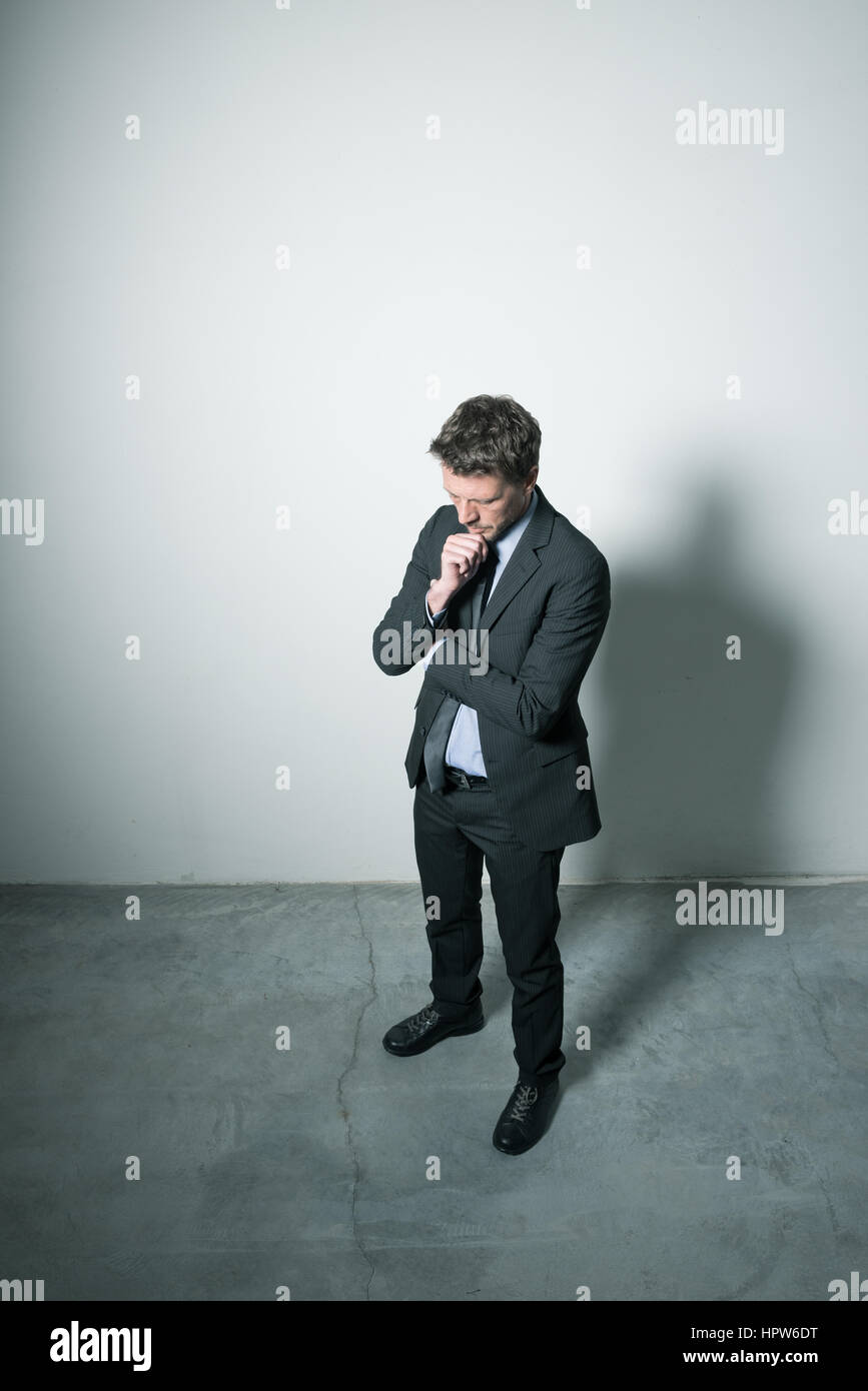 Businessman standing with hand on chin à l'obscurité dans une chambre vide. Banque D'Images Businessman standing with hand on chin à l'obscurité dans une chambre vide. Banque D'Images