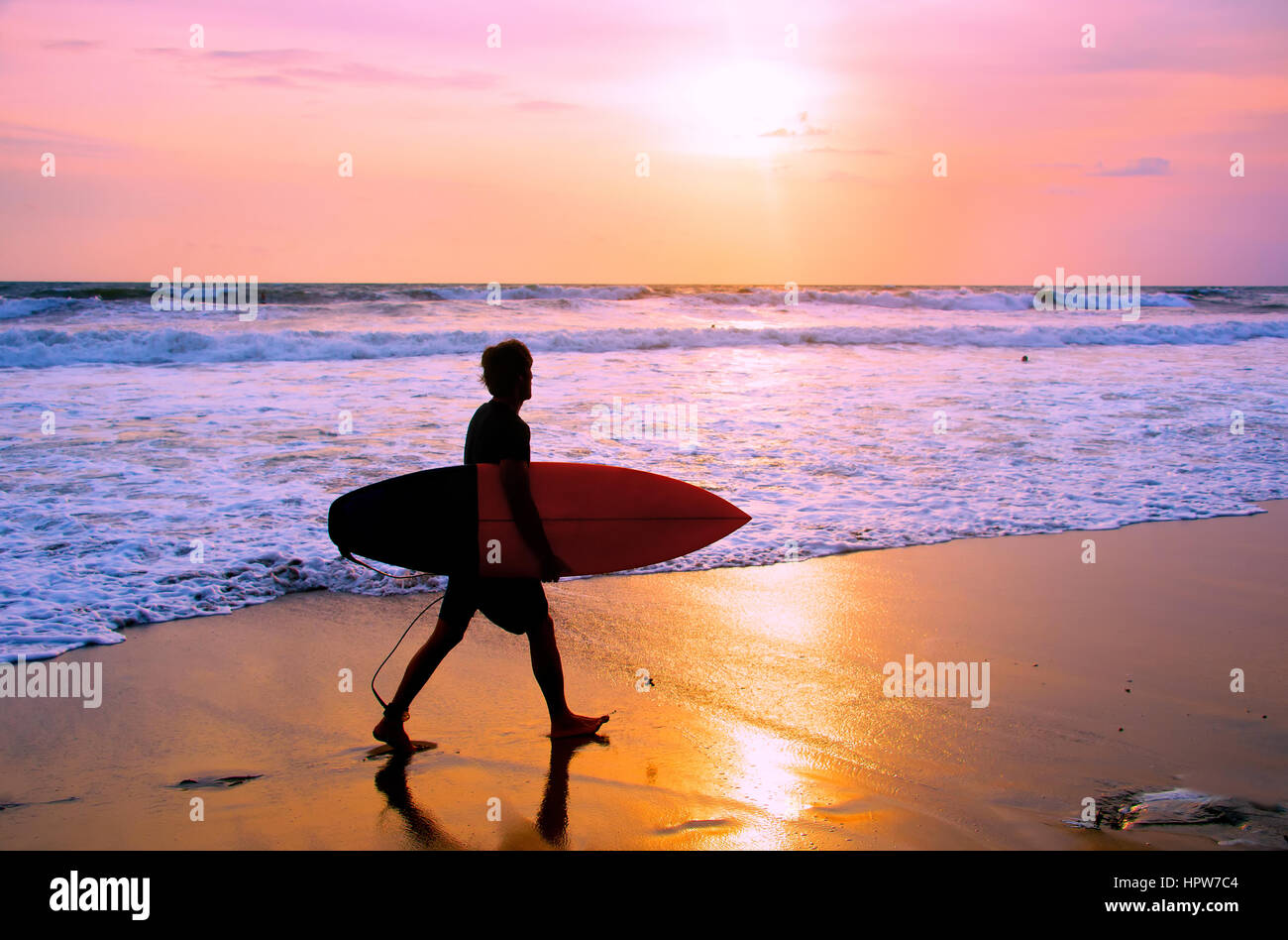Surf surfer avec la marche sur la plage au coucher du soleil. L'île de Bali, Indonésie Banque D'Images