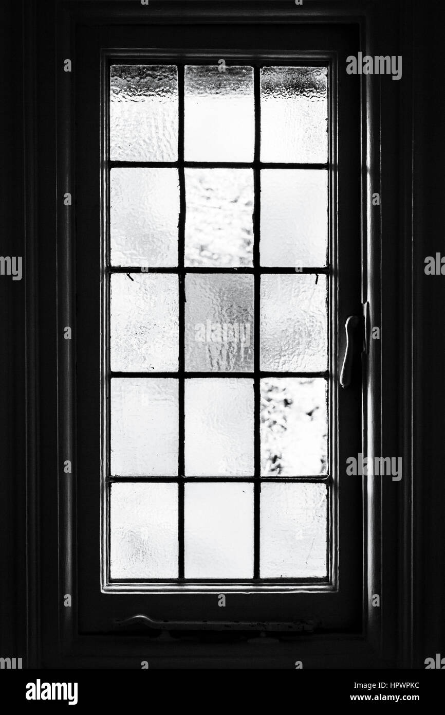 Image en noir et blanc d'une fenêtre en verre dépoli de boiseries provenant de l'intérieur, avec son surround sombre Banque D'Images