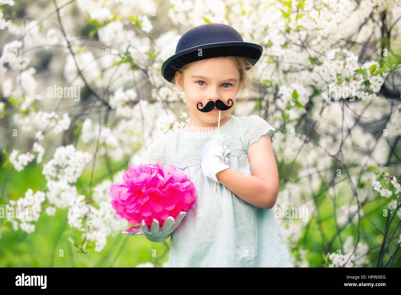 Funny Girl en chapeau et des gants et avec fake moustache jouant dans le jardin de printemps. Banque D'Images