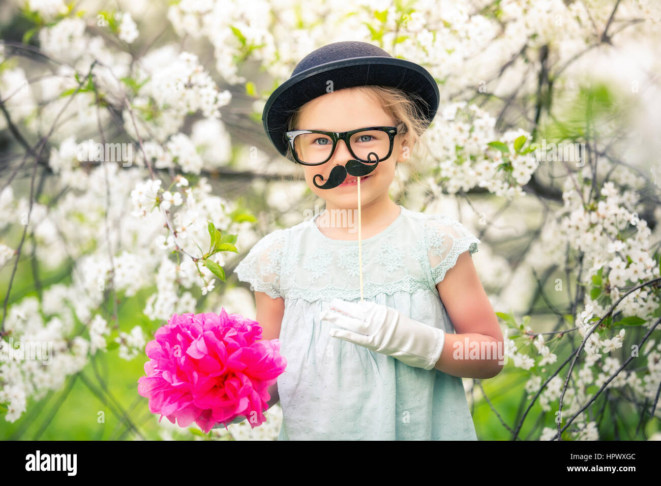 Funny Girl avec chapeau, lunettes et gants et avec fake moustache jouant dans le jardin de printemps. Banque D'Images