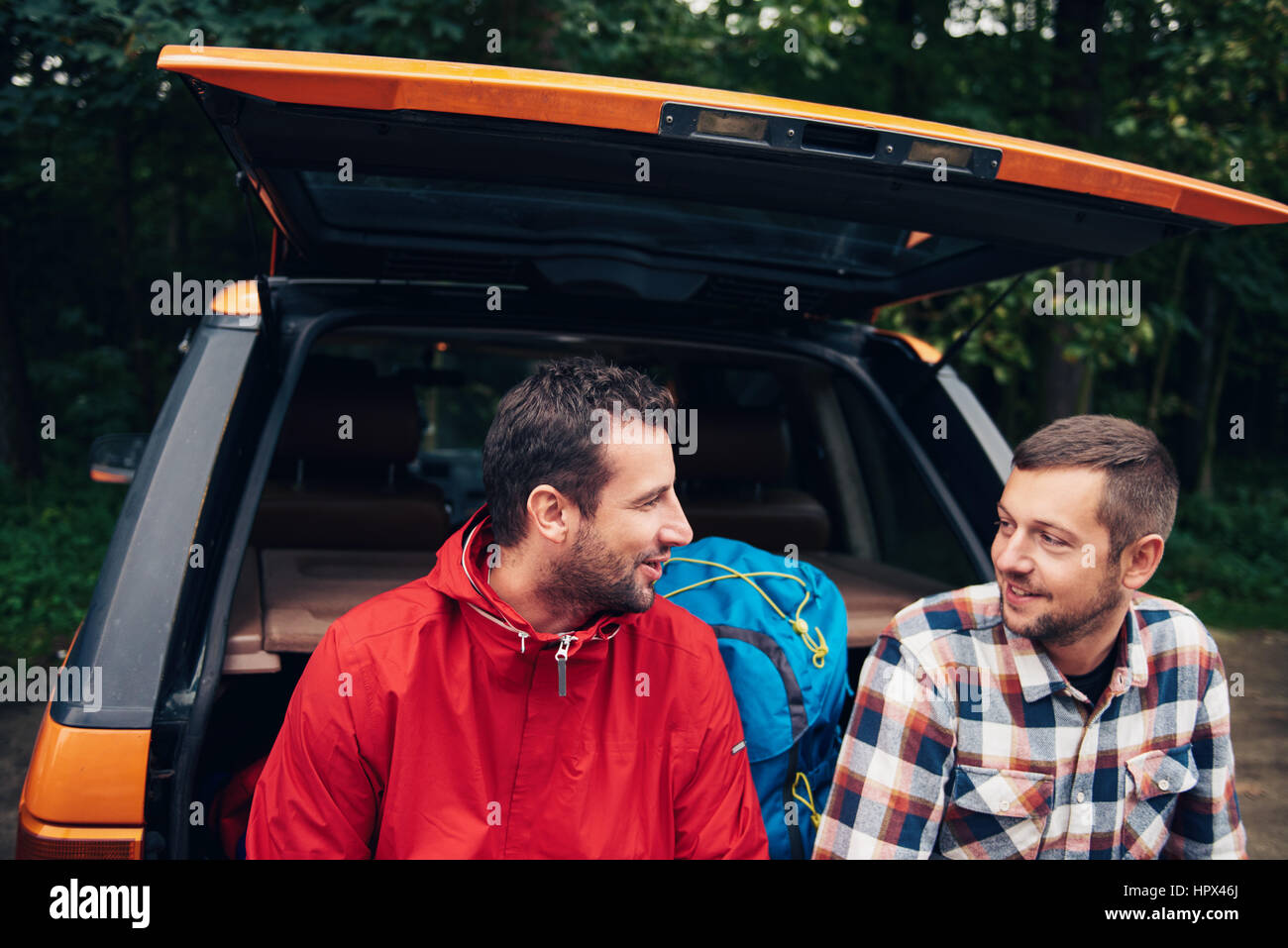 Deux hommes parlant ensemble tout en restant assis à l'arrière d'un véhicule plein de matériel de randonnée prêt à partir pour un trek dans la nature Banque D'Images