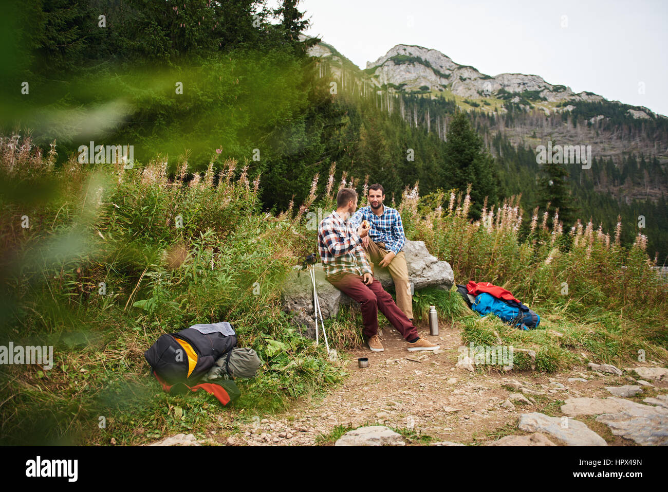 Deux jeune homme assis sur un rocher avec leur matériel de randonnée de manger des collations tout en prenant une pause de trekking dans les montagnes Banque D'Images