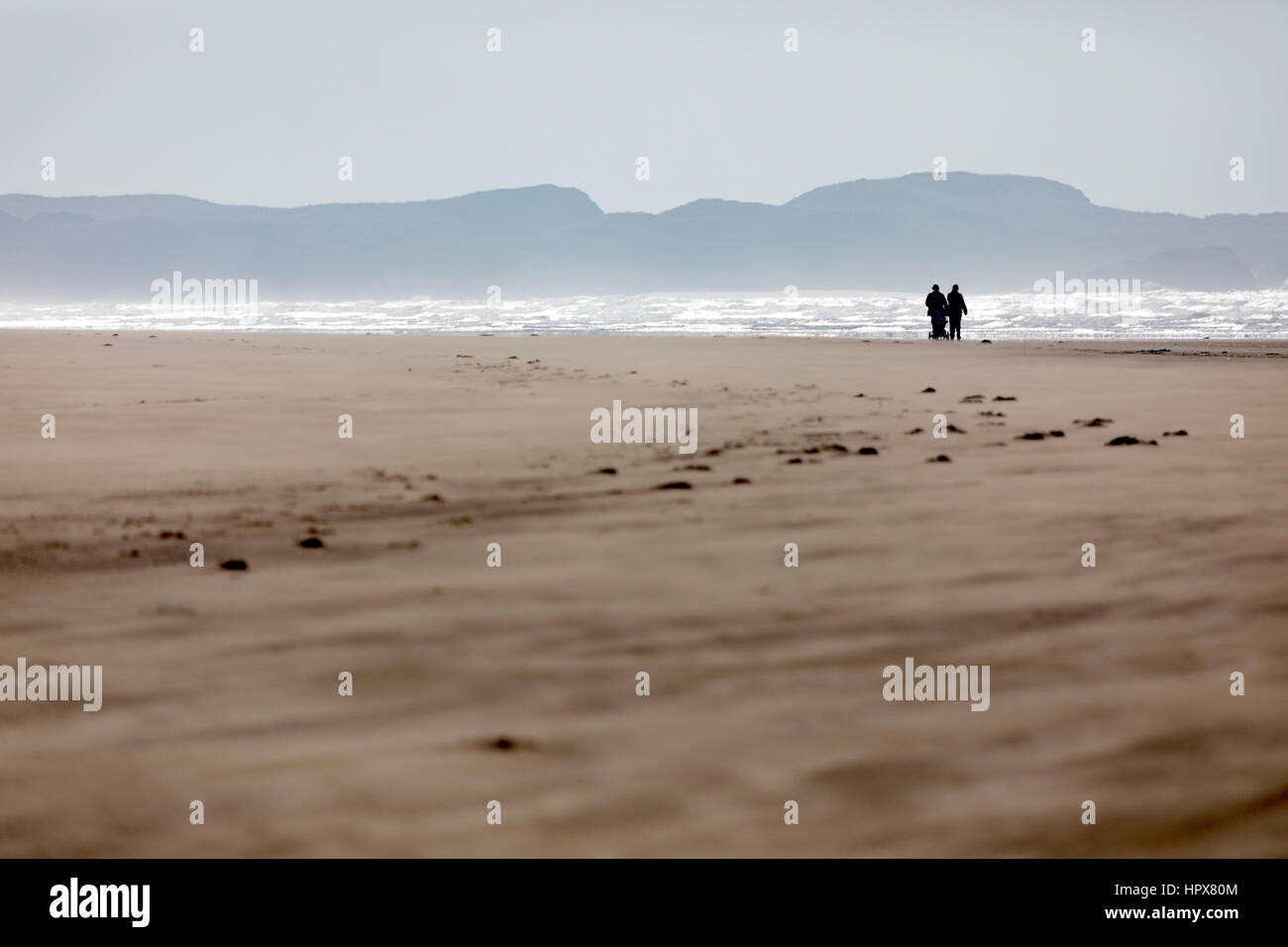 Un couple avec un landau à marcher le long de la plage déserte à Anglesey, au Pays de Galles sur Newborough Banque D'Images