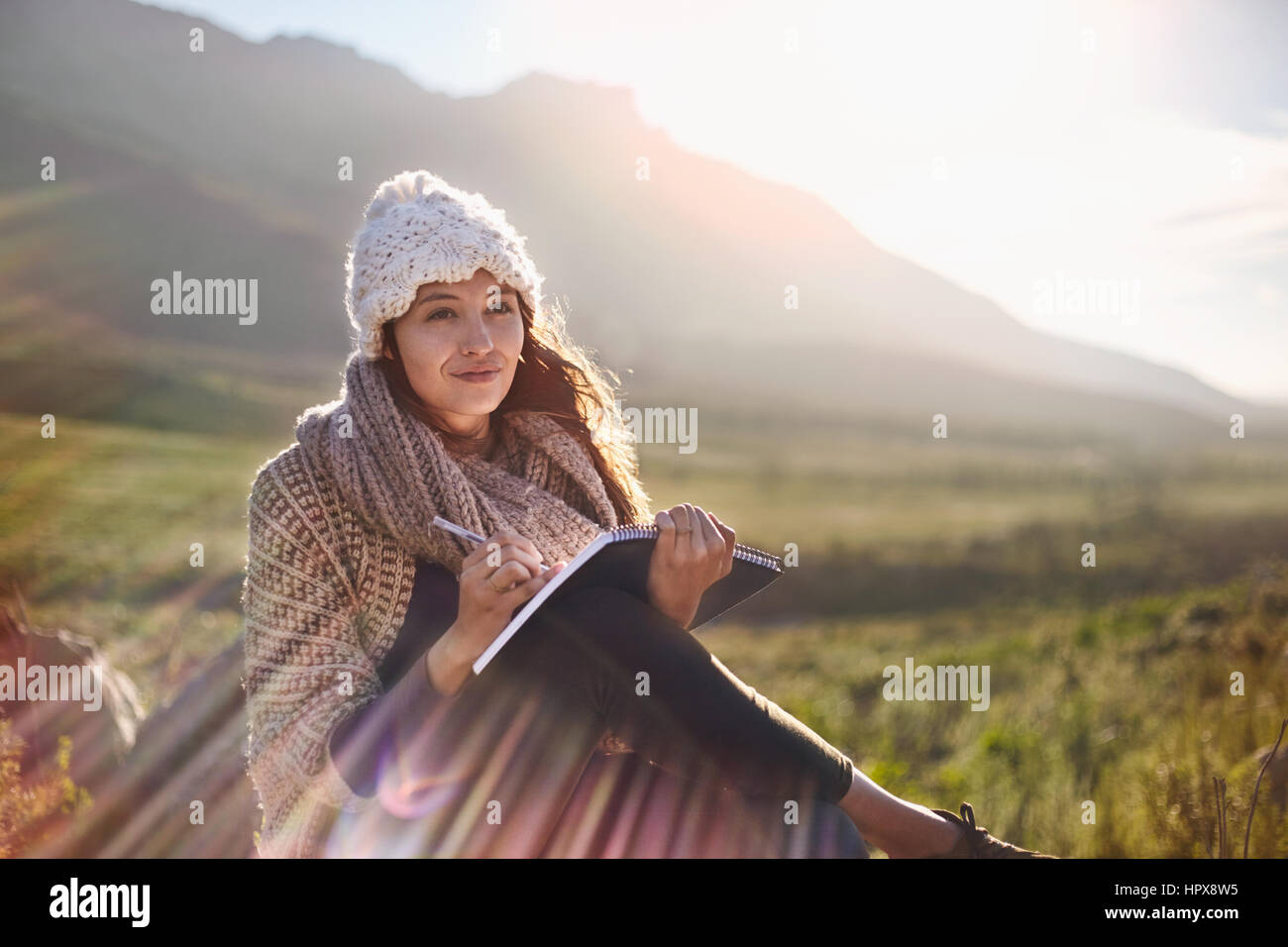 Jeune femme écrivant dans le journal sous le soleil, sur le terrain à distance Banque D'Images