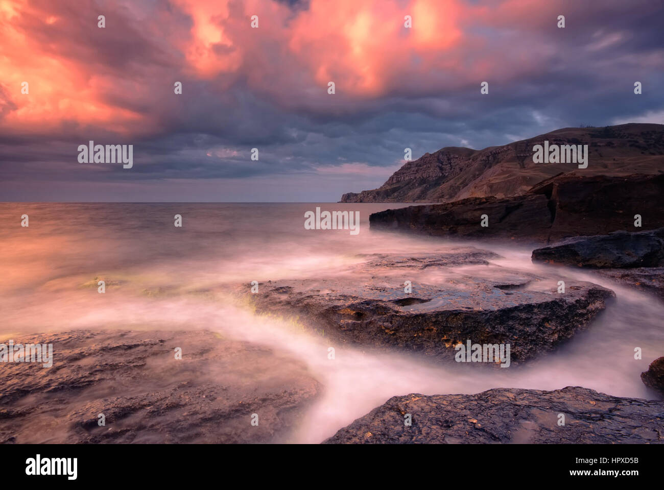 La mer des rochers dans l'eau lisse avec orange ciel nuages Banque D'Images