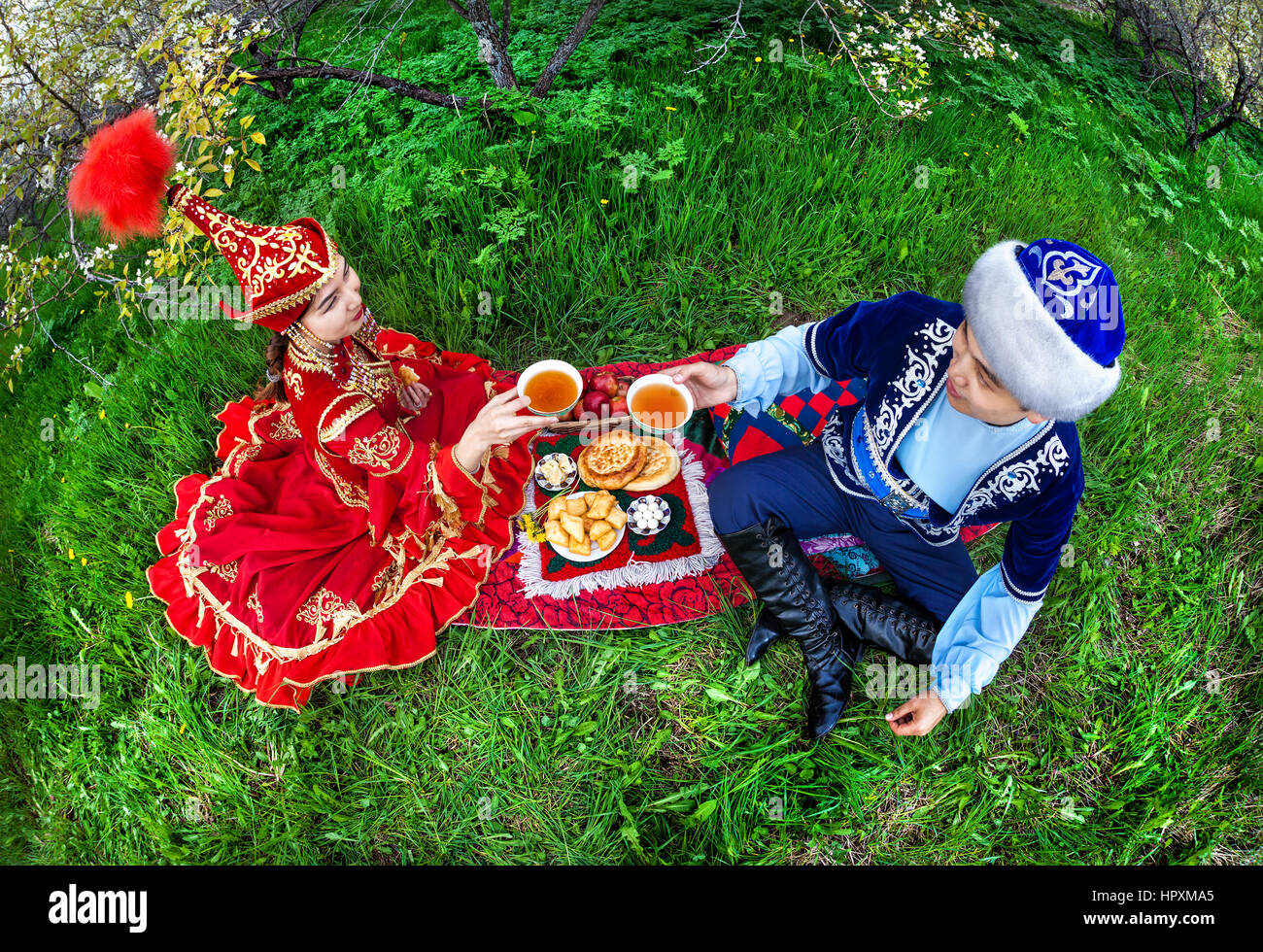 Couple en costume Kazakh assis dans le jardin en fleurs du printemps à Apple de pique-nique et de boire le thé à Almaty, Kazakhstan, en Asie centrale Banque D'Images