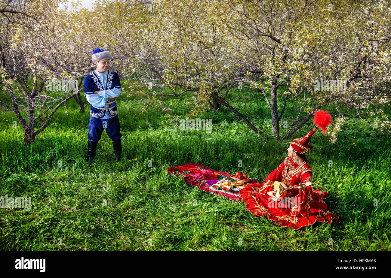 Couple en costume Kazakh au printemps fleurs jardin apple à pique-nique avec dombra à Almaty, Kazakhstan, en Asie centrale Banque D'Images