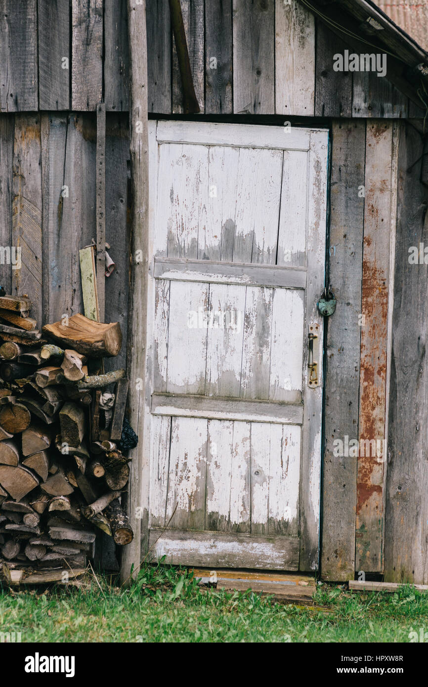 La porte de l'ancienne grange avec décollement de peinture blanche. Près de  jeter les bois empilés dans un tas. Porte fermée sur le verrou Photo Stock  - Alamy