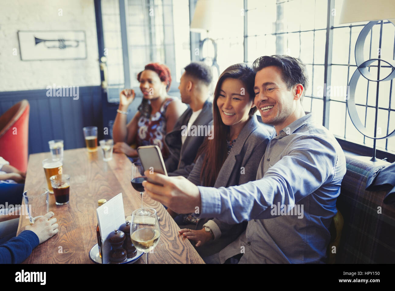 Smiling couple en tenant avec selfies téléphone appareil photo à table en bar Banque D'Images
