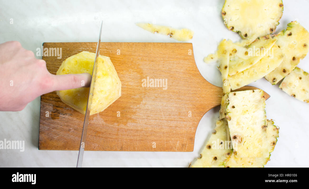 Les mains des hommes d'ananas frais de coupe sur une planche en bois Banque D'Images