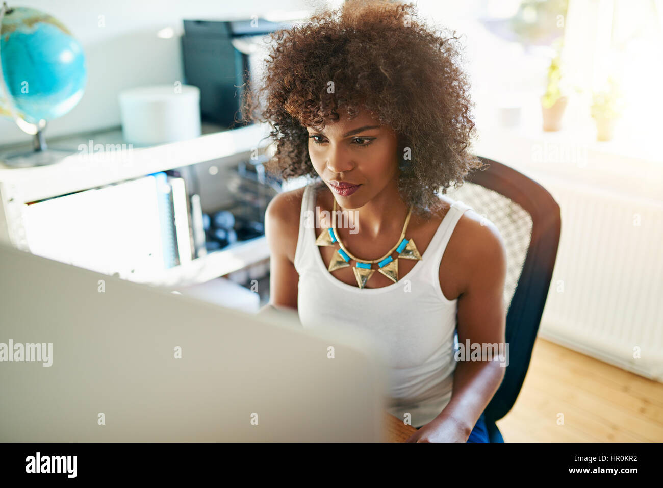 Attractive African American businesswoman assise à son ordinateur dans une grande clé office travaillant sur un grand moniteur de bureau Banque D'Images