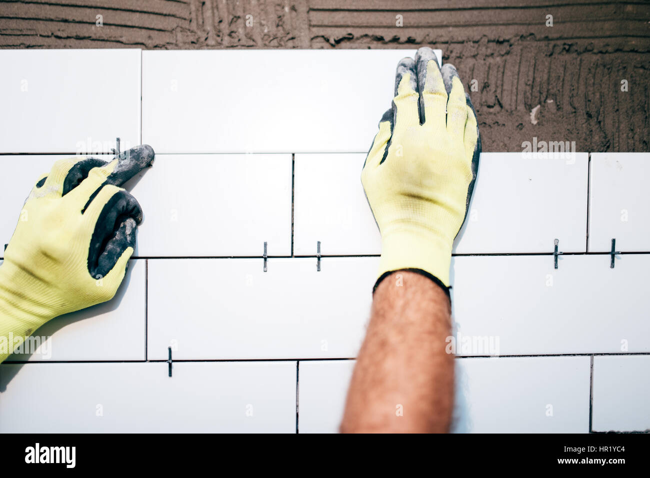 Travailleur industriel, les mains de l'installation des carreaux de céramique sur les murs intérieurs, un homme à l'aide de film plastique distancer pour le réglage de tuiles. Détails de Construction Banque D'Images