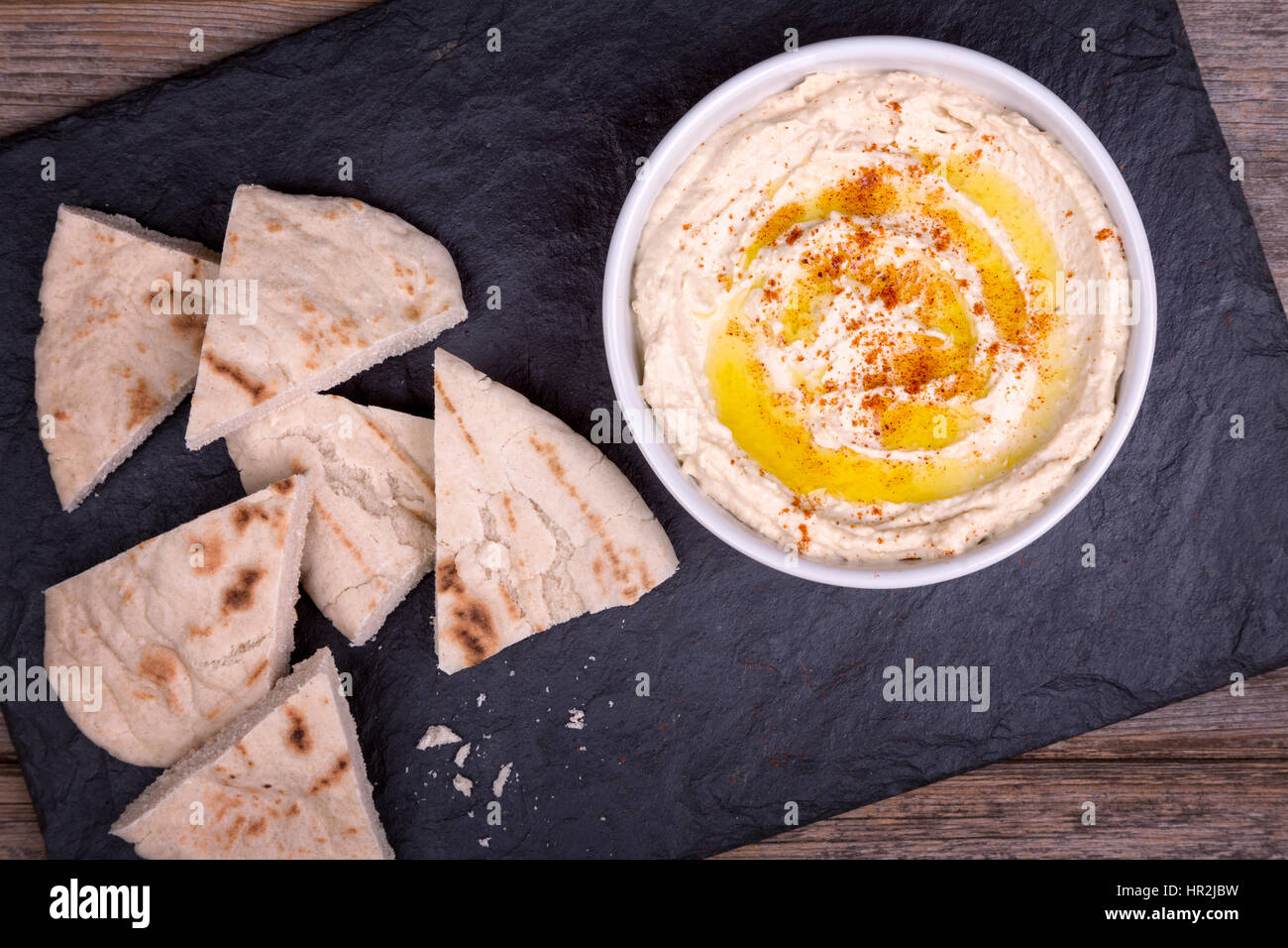 Un bol d'hoummos frais, arrosé d'huile d'olive et paprika, servi avec des quartiers de pain pita. Banque D'Images