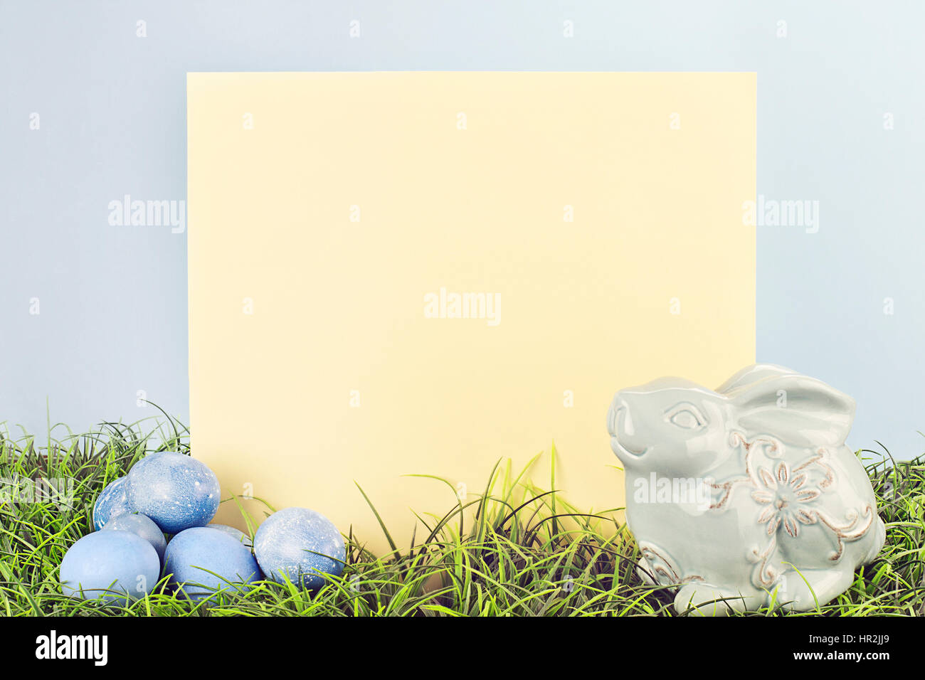Signe avec copie espace vide avec des oeufs de Pâques teints et un générique bunny dans l'herbe sur un fond bleu. Banque D'Images