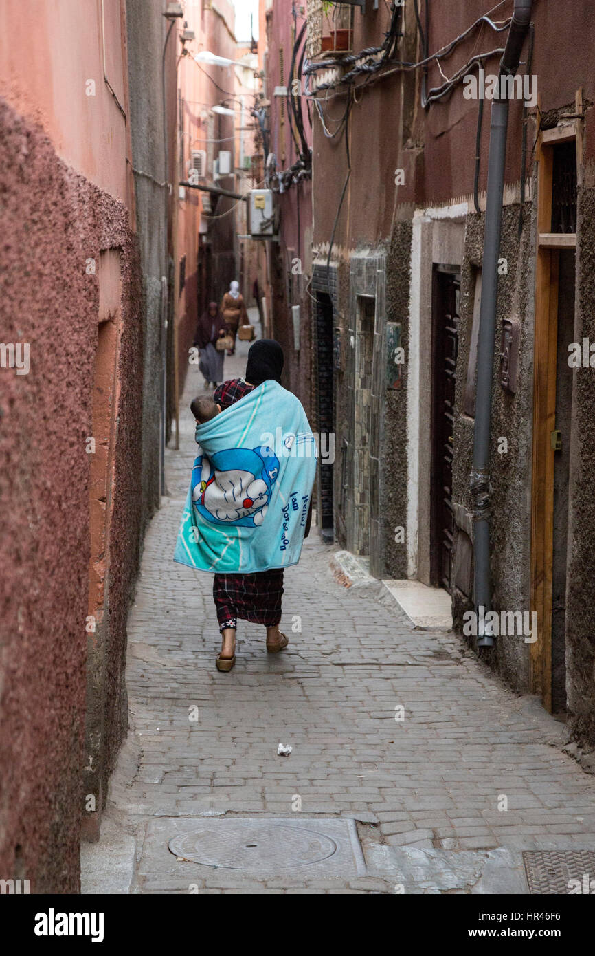 Marrakech, Maroc. Femme transportant bébé sur son dos dans une ruelle de la médina. Banque D'Images