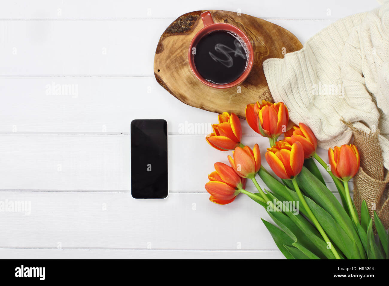 Les frais généraux ont tiré sur un téléphone avec une tasse de café chaud et un bouquet de fleurs tulipes avec une agréable knit jeter couverture sur table en bois blanc dessus. Télévision jeter top v Banque D'Images