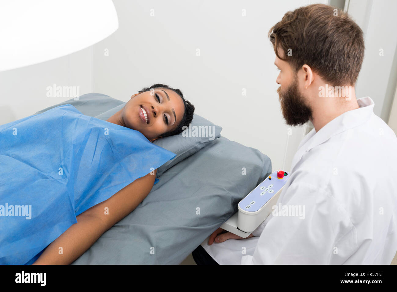 Portrait of smiling patient allongé sur le lit tout en séance par son médecin en clinique Banque D'Images