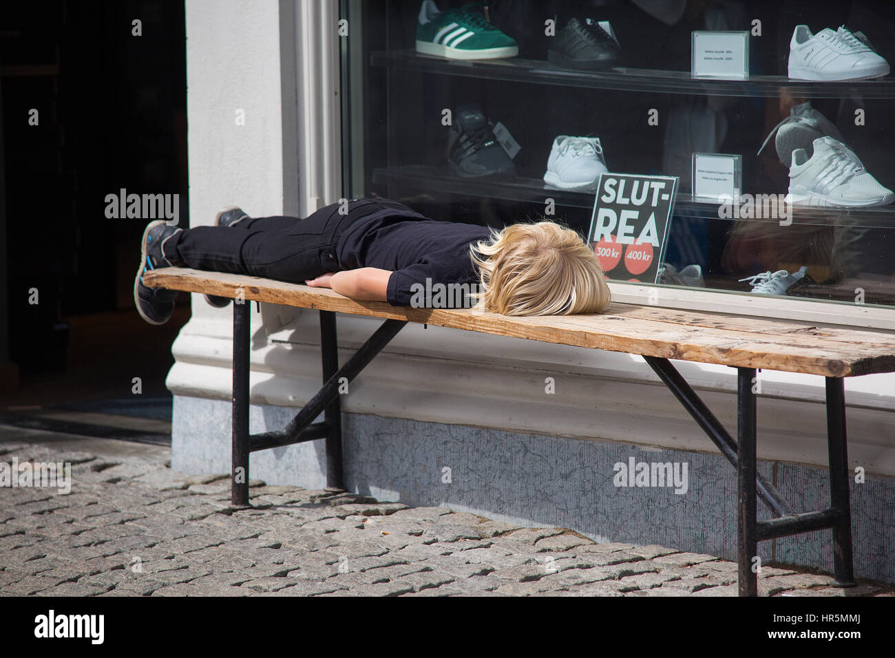 Enfant couché sur un banc à l'extérieur d'un magasin de l'espadrille. Banque D'Images