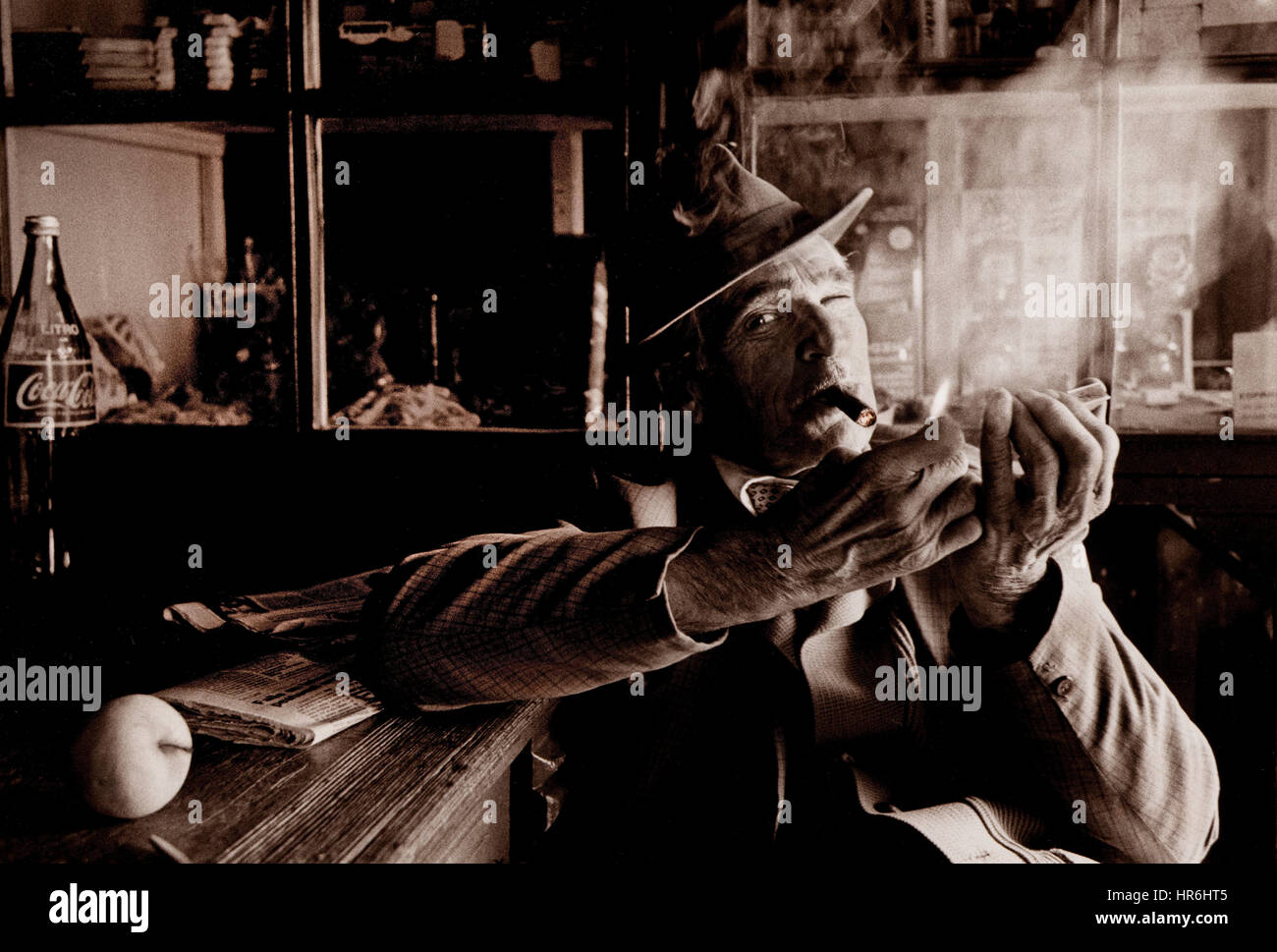 Frappez un cigare mûr dans un bar rustique photographié sur le film Kodak tri-X rétro reportage étude de l'homme espagnol mature avec chapeau éclairant un cigare dans un bar local Banque D'Images