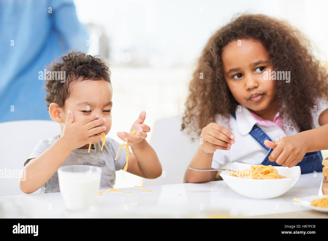 Mignon bébé garçon et sa jolie soeur avec de longs cheveux bouclés assis à table de dîner et manger de délicieux pâtes aux mains Banque D'Images