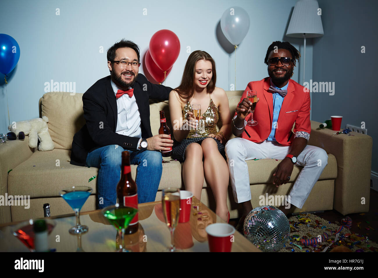 Deux hommes barbus avec bouteille de bière et champagne flute looking at camera while leur jolie femme ami assis entre eux Banque D'Images