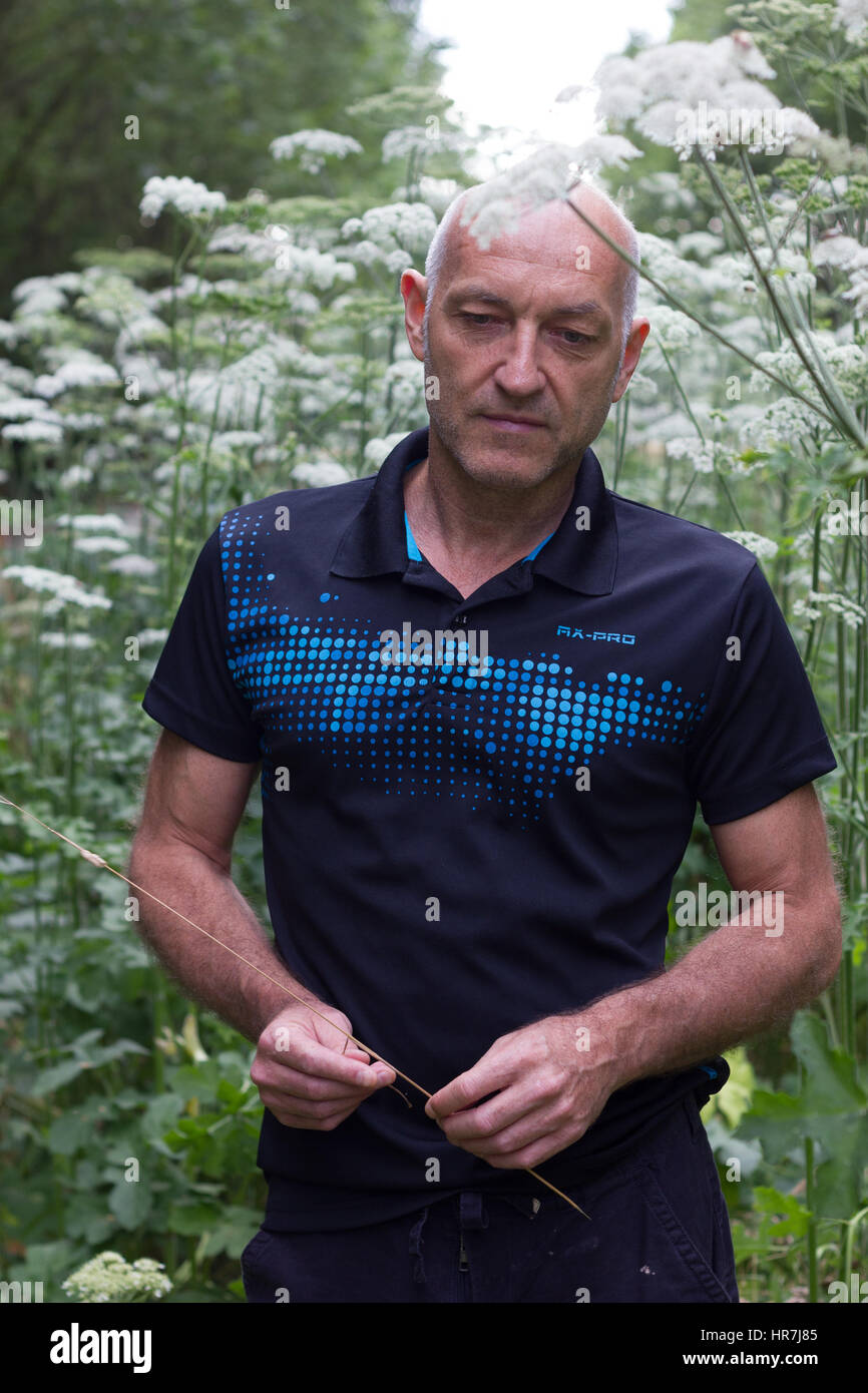 Portrait d'un homme chauve qui pose en face de fleurs avec une tige dans la main Banque D'Images