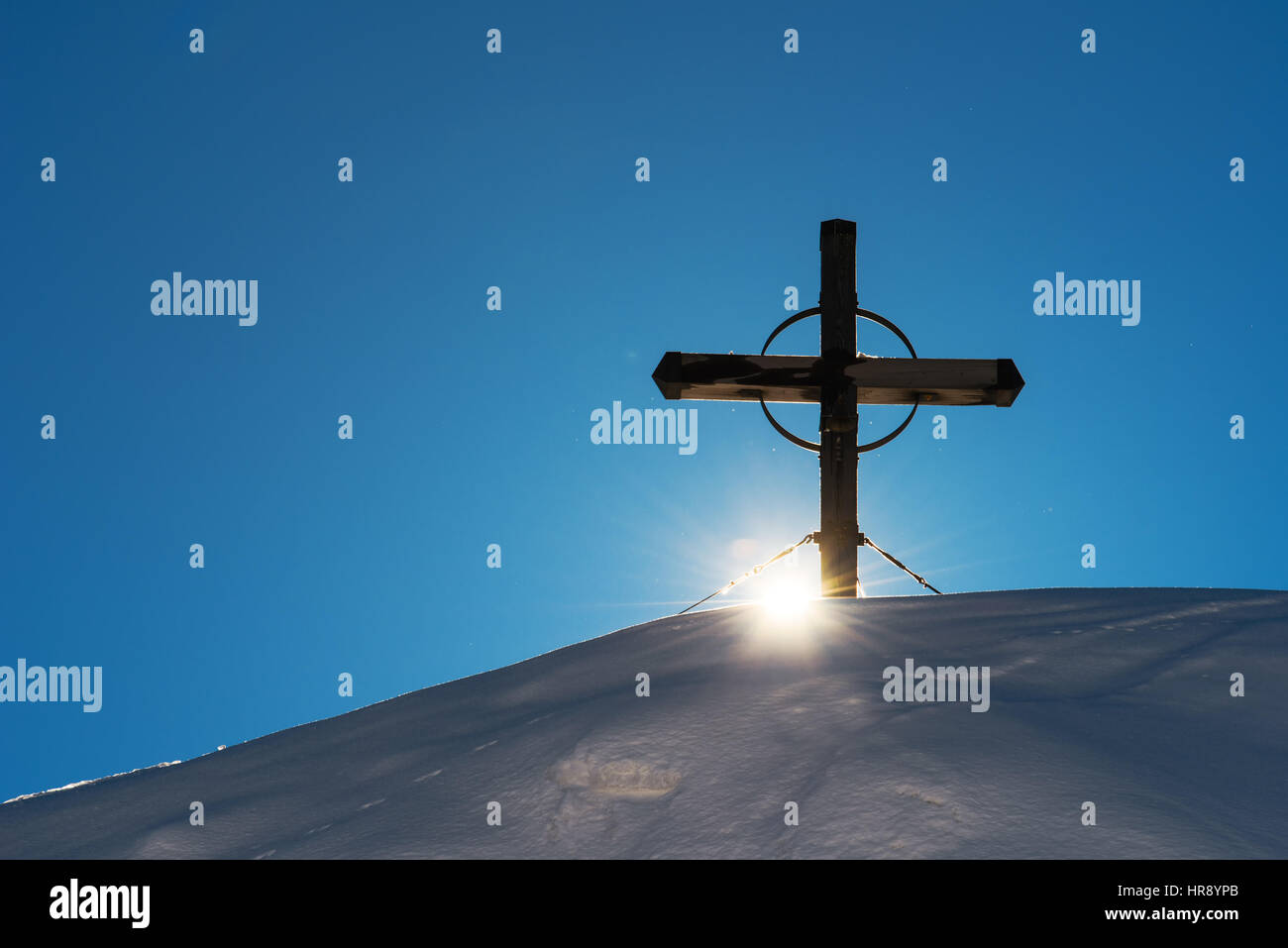 Croix de bois sur la colline de montagne enneigées, soleil rayonnant à travers Banque D'Images