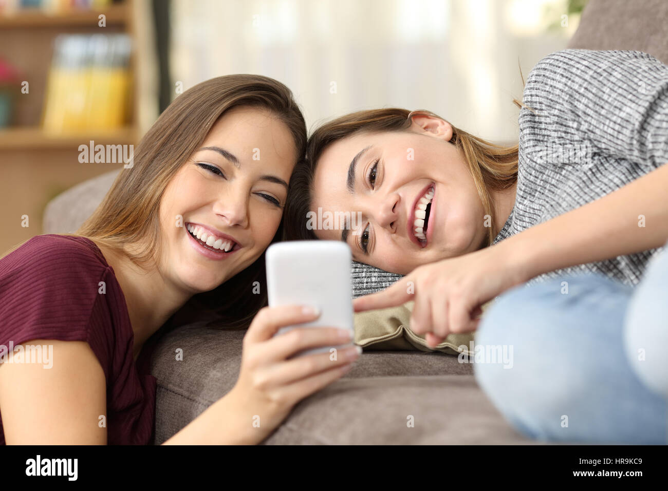 Colocation heureux d'avoir l'oeil sur le contenu en ligne dans un téléphone intelligent allongé sur un canapé dans la salle de séjour à la maison Banque D'Images