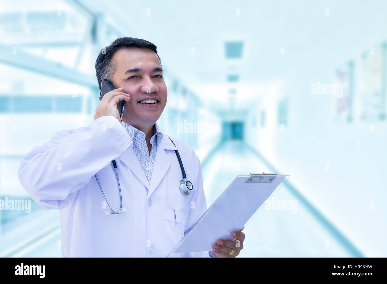 Médecin homme asiatique avec un sourire heureux en utilisant un smartphone sur fond blanc floue Banque D'Images