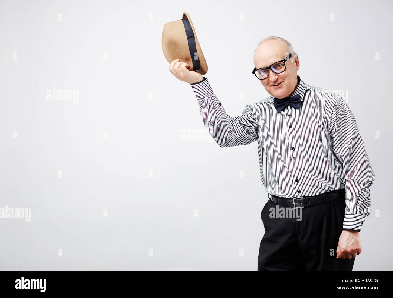 Portrait de l'homme retraite élégante en soirée et en tenant son chapeau melon et souriant gaiement isolé sur fond blanc Banque D'Images