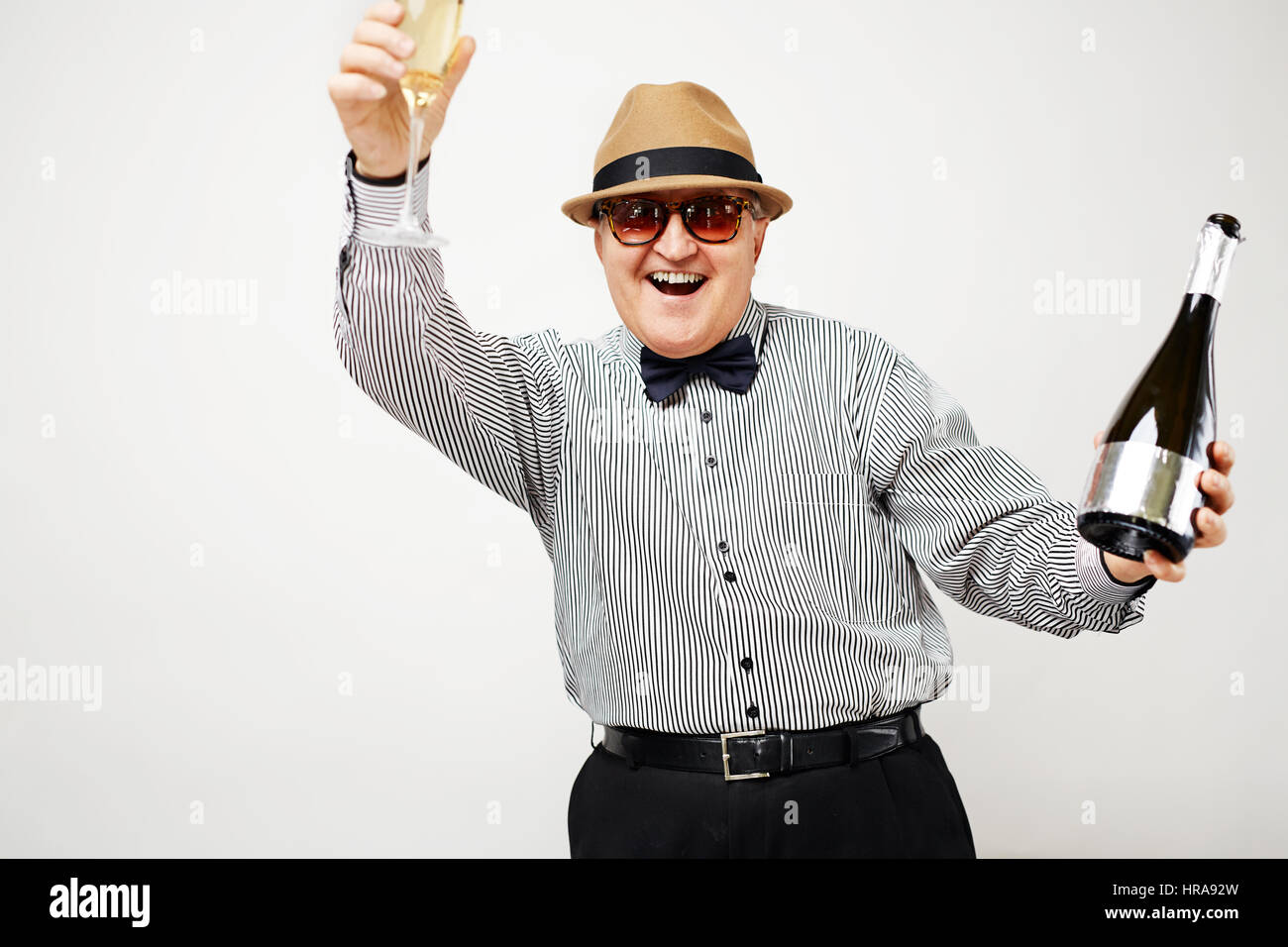 Portrait of happy dressed-up pensionné ayant l'amusement et l'éducation d'un verre de champagne contre mur blanc Banque D'Images