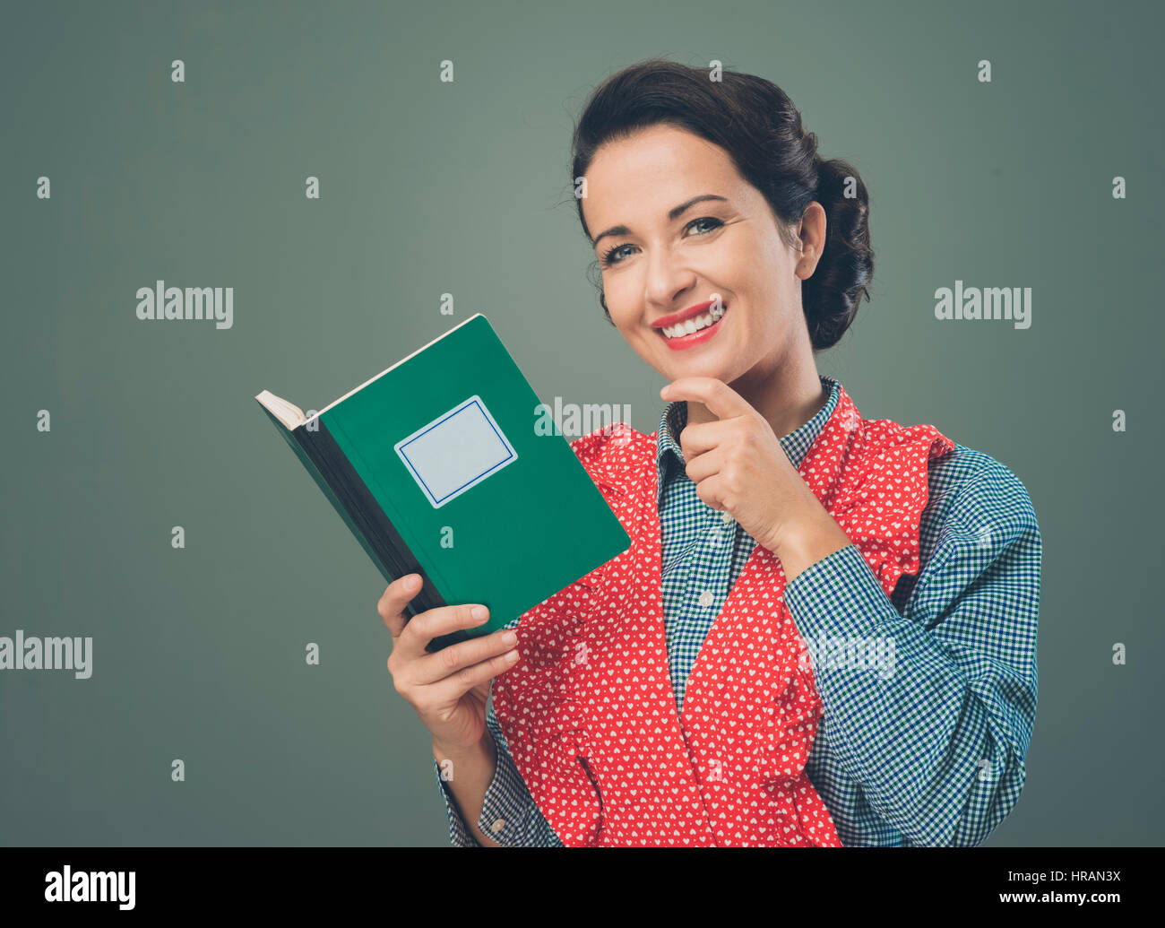 Rétro femme en souriant avec tablier et livre de hand on chin Banque D'Images Rétro femme en souriant avec tablier et livre de hand on chin Banque D'Images