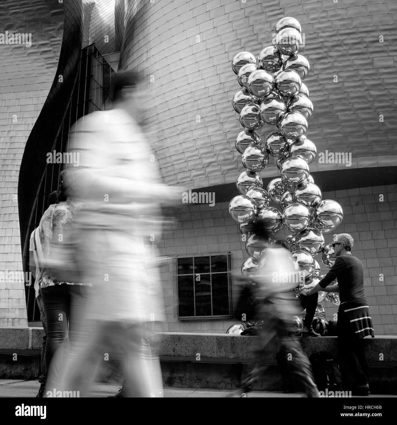 L'homme en passant en face du grand tas de bulles d'argent brillant et les passants en premier plan en noir en blanc Banque D'Images