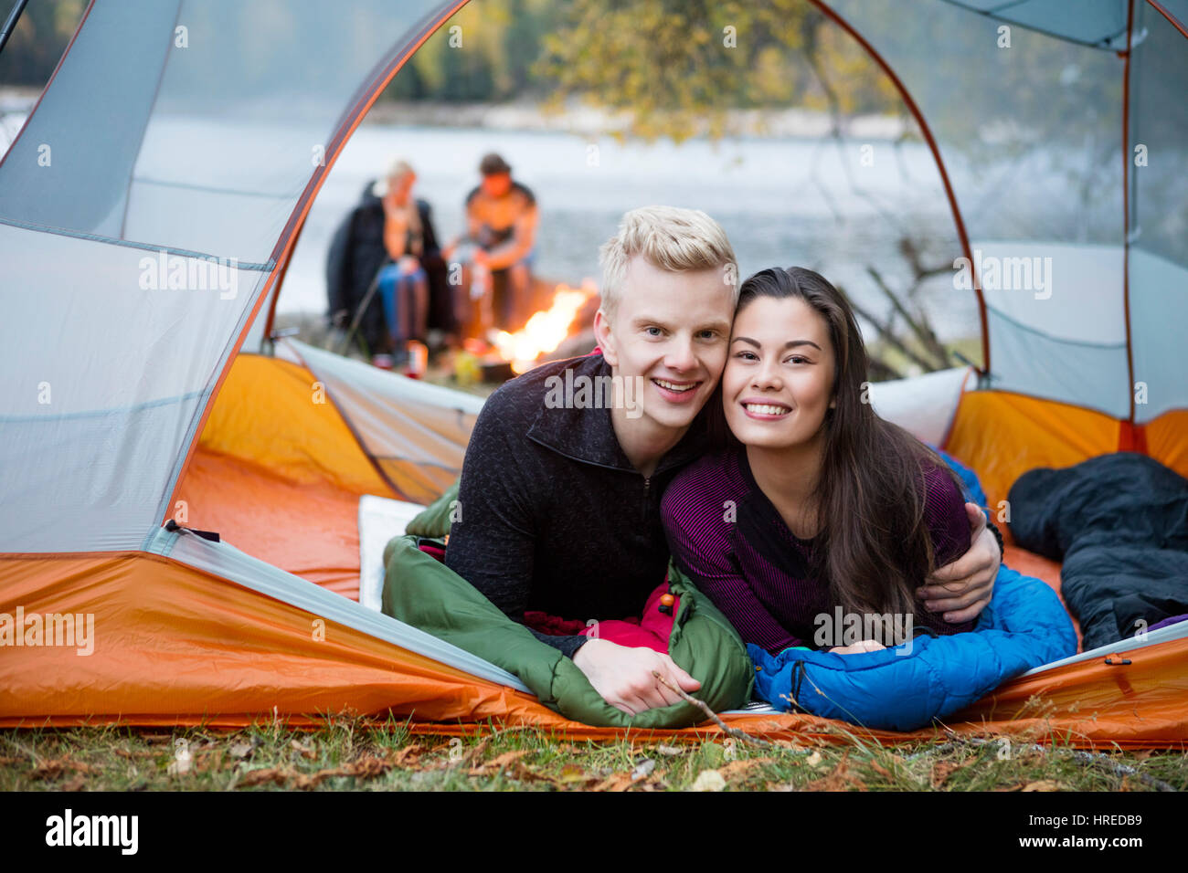 Portrait de l'amour jeune couple couché dans la tente avec des amis en arrière-plan au Lakeshore Banque D'Images