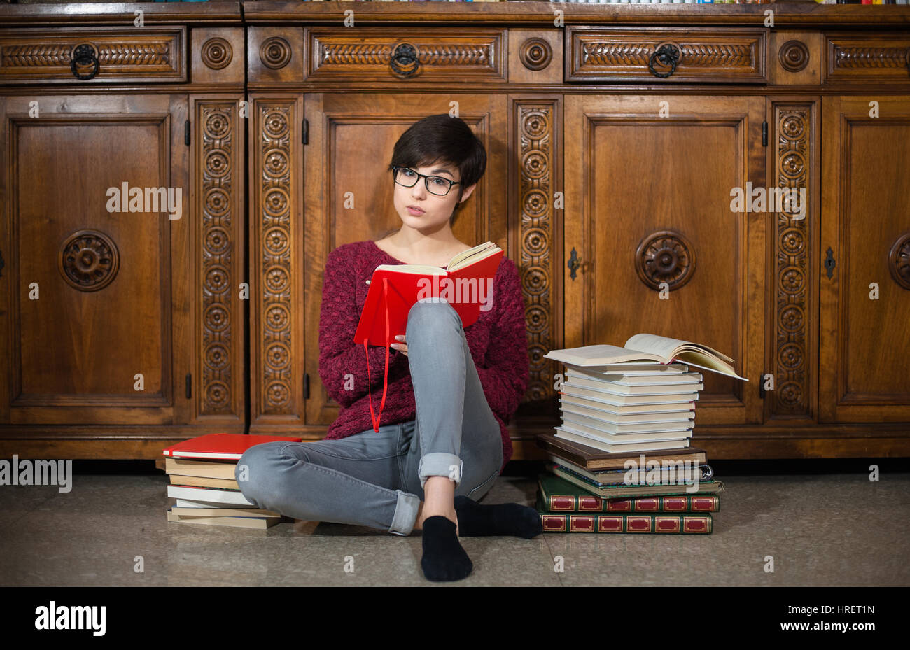 Jeune étudiante avec expression visage fatigué à la caméra à tout en étant assis sur le sol avec de nombreux livres autour de Banque D'Images