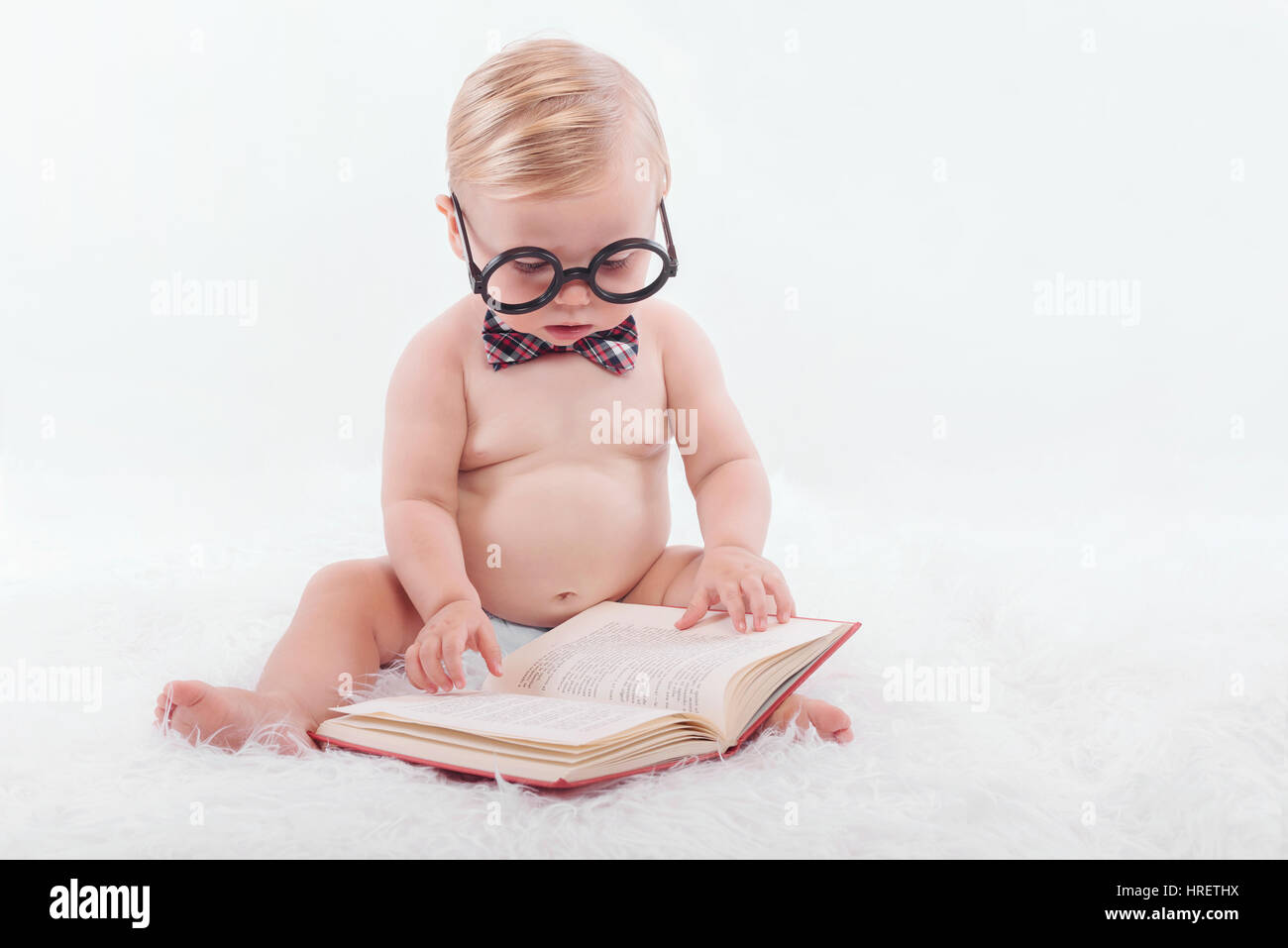 Petit bébé heureux de lire un livre avec des lunettes et une cravate Banque D'Images